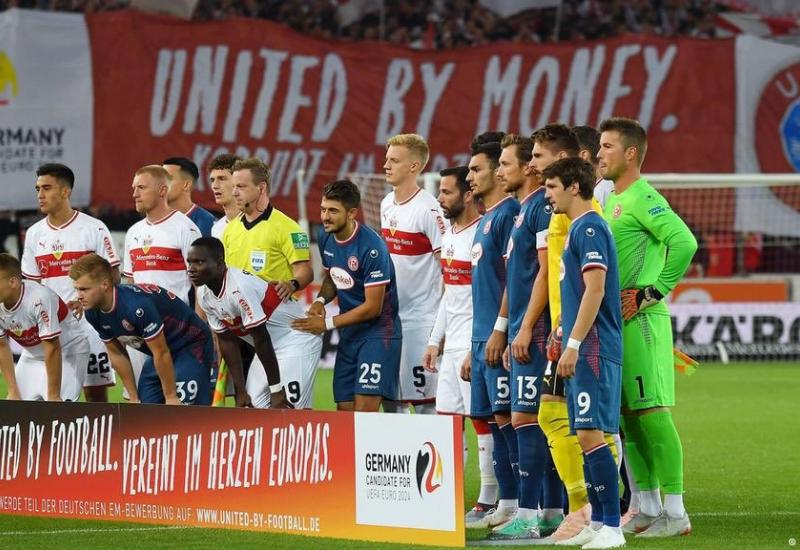 Igrači VfB Stuttgart i Fortuna Düsseldorf iza kojih se vidi veliki transparent - Navijači u Njemačkoj protiv kandidature njihove zemlje za EURO 2024