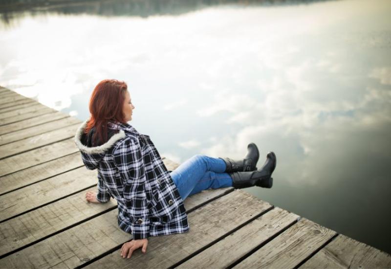 Žena sjedi uz rijeku - Otkrivamo 10 dobrobiti koje tišina ima na naše zdravlje