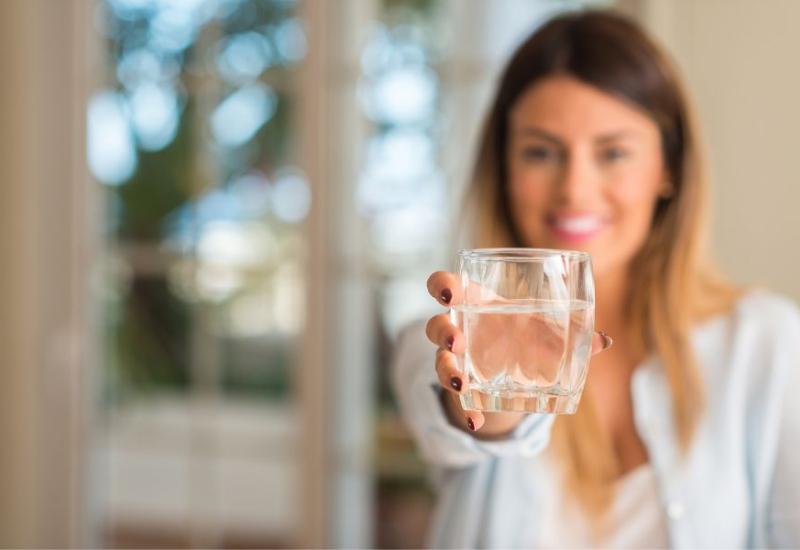 Žena s čašom vode - Nutricionisti otkrivaju 7 najboljih pića za ublažavanje nadutosti